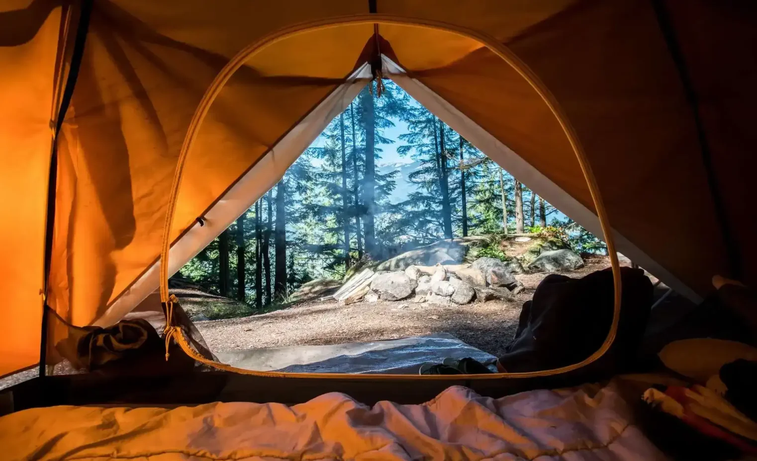 orange dome tent pitched on a hillside with a rental sleeping bag.webp